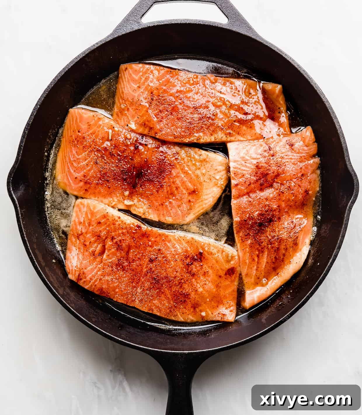 Sticky Honey Garlic Salmon 6 Four salmon fillets being seared in a black skillet with the sauce.