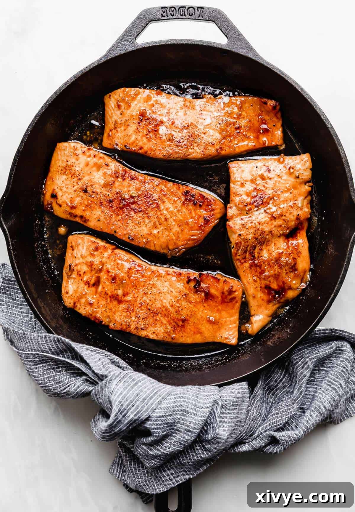 Sticky Honey Garlic Salmon 7 Four Honey Garlic Baked Salmon fillets in a cast iron pan, showing the sauce being spooned over.