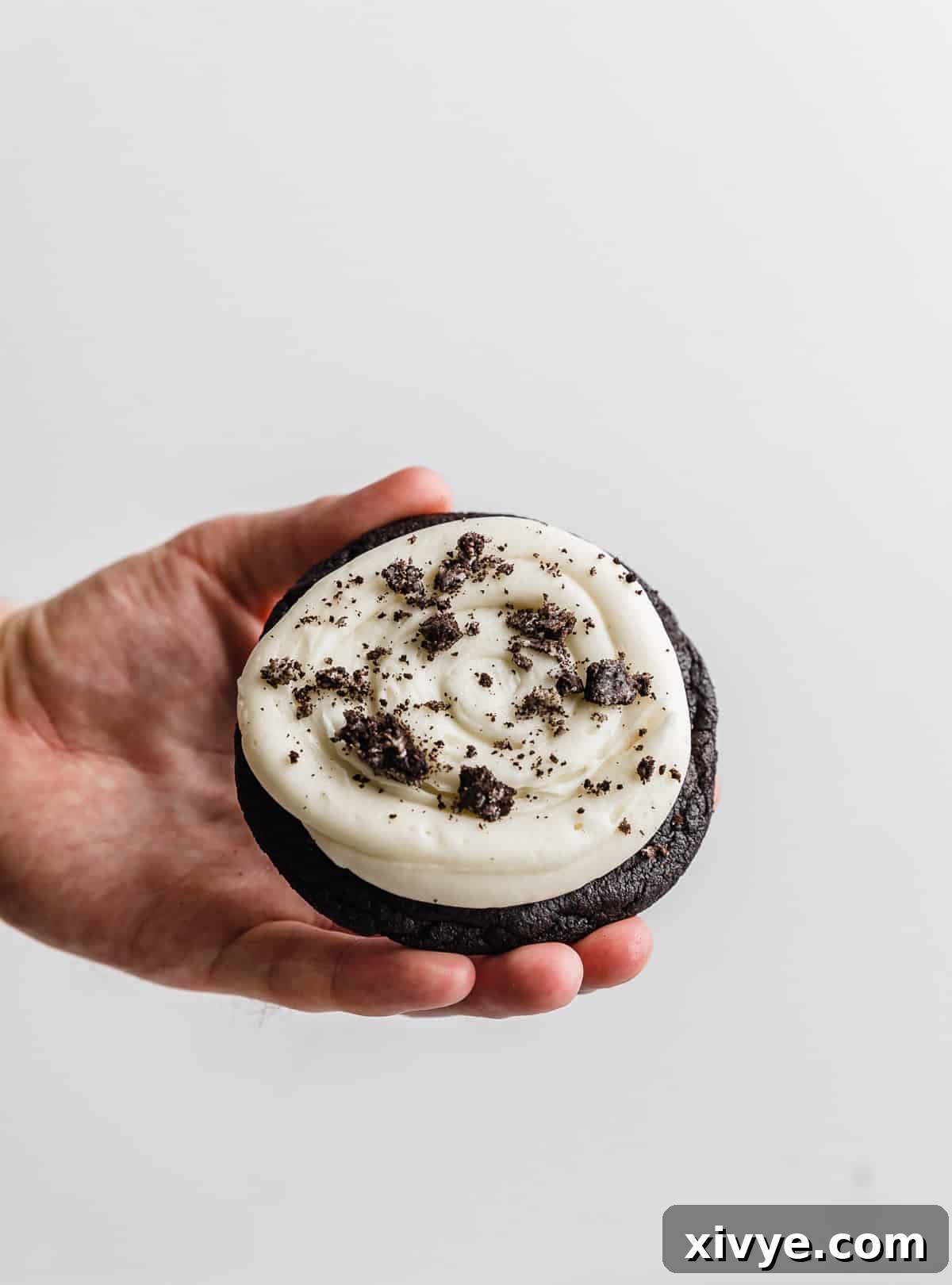 Giant Crumbl Style Chocolate Oreo Cookies 13 A hand holding up a Chocolate Oreo Crumbl Cookie against a white background.