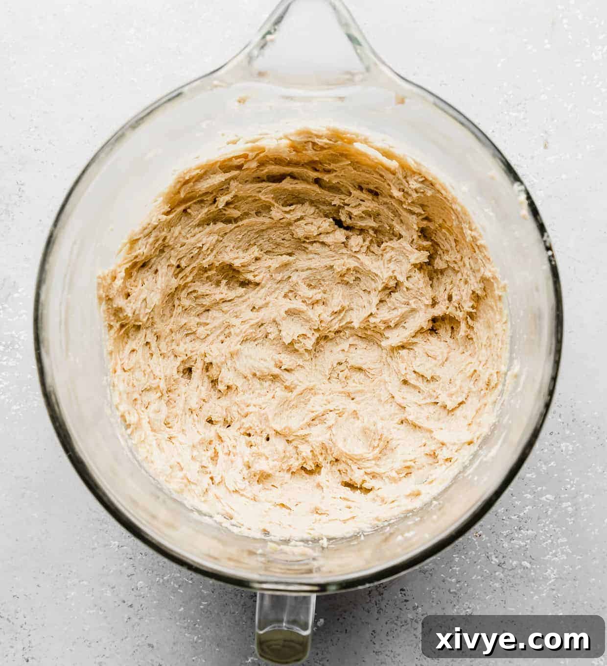 Giant Crumbl Style Chocolate Oreo Cookies 8 Creamed butter, sugar, eggs, and vanilla in a glass mixing bowl on a light gray background.