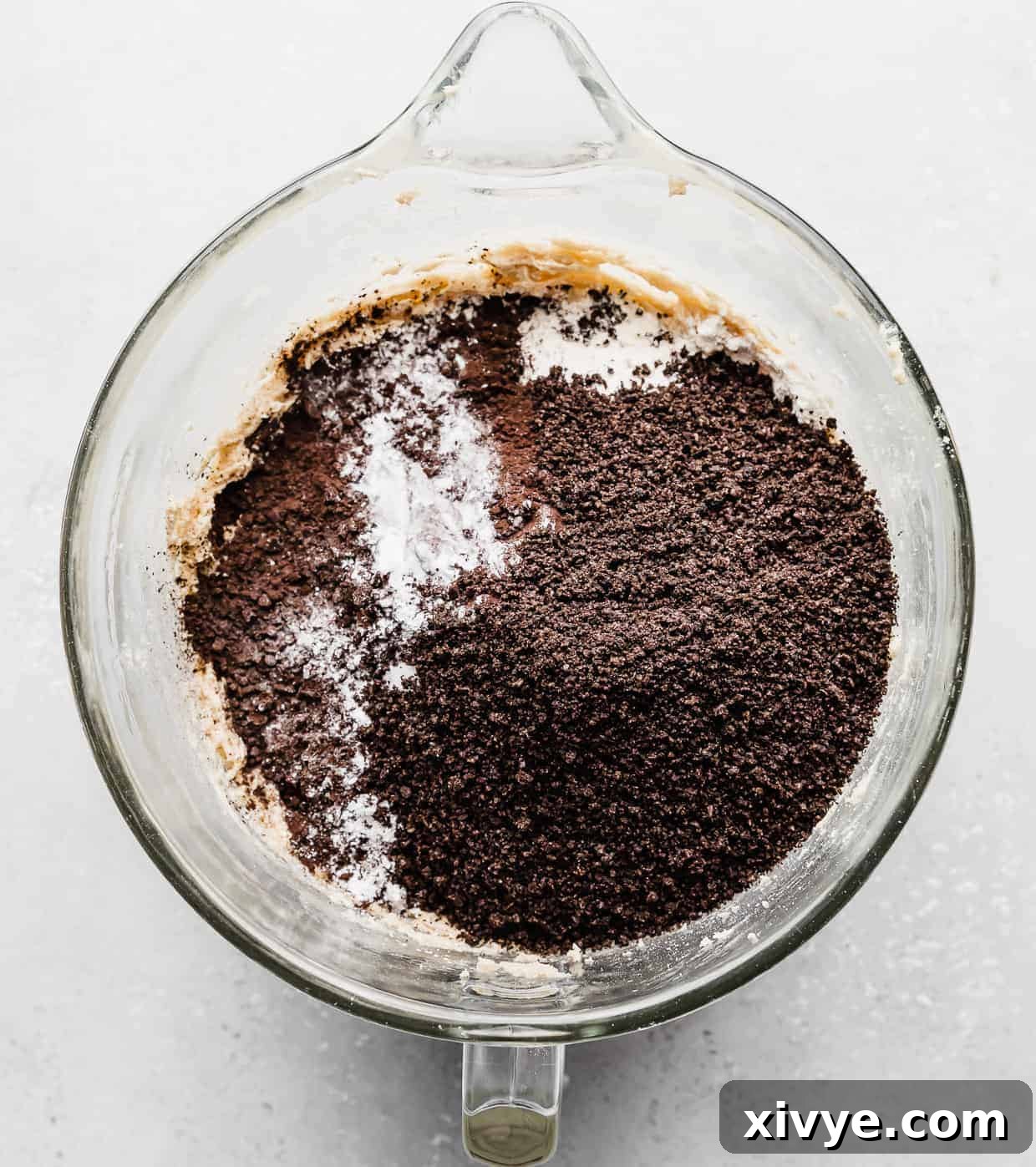 Giant Crumbl Style Chocolate Oreo Cookies 9 A mixing bowl with crushed Oreos, black cocoa powder, and flour overtop creamed butter.