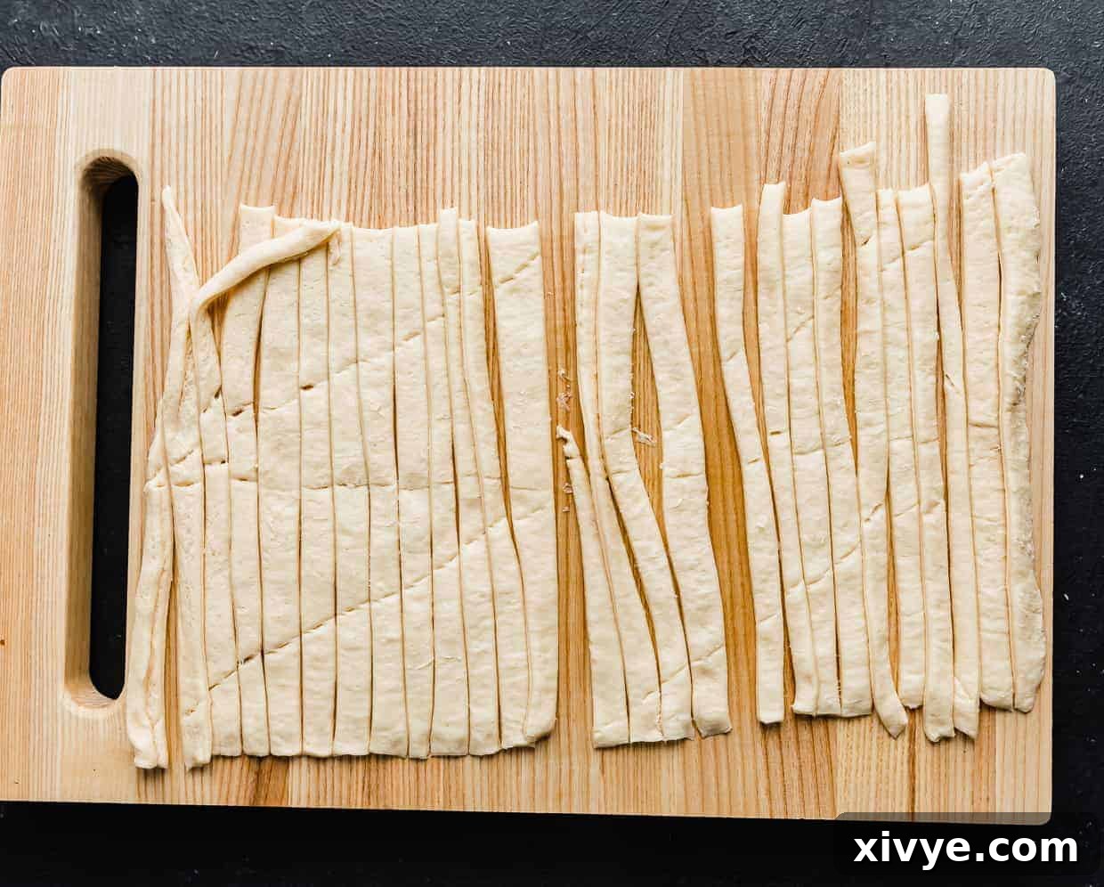 Creepy Canine Wraps 5 A wooden cutting board with a crescent roll sheet cut into strips on it.