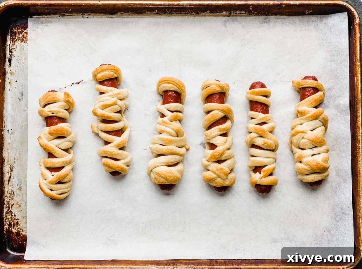 Creepy Canine Wraps 7 Baked Mummy Hot Dogs on a baking sheet.