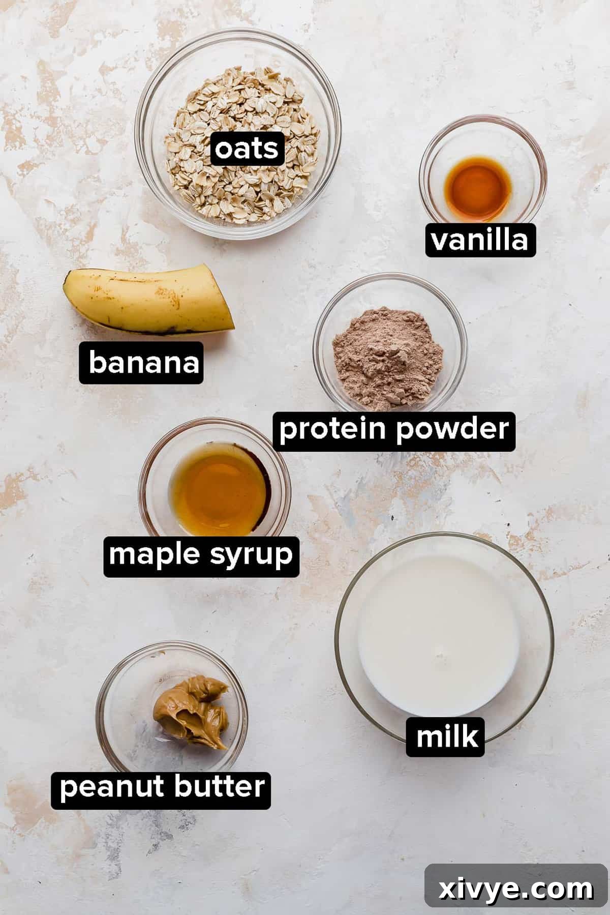 Powerhouse Protein Oats 3 High Protein Overnight Oats ingredients in a glass bowl on a textured white and cream background.