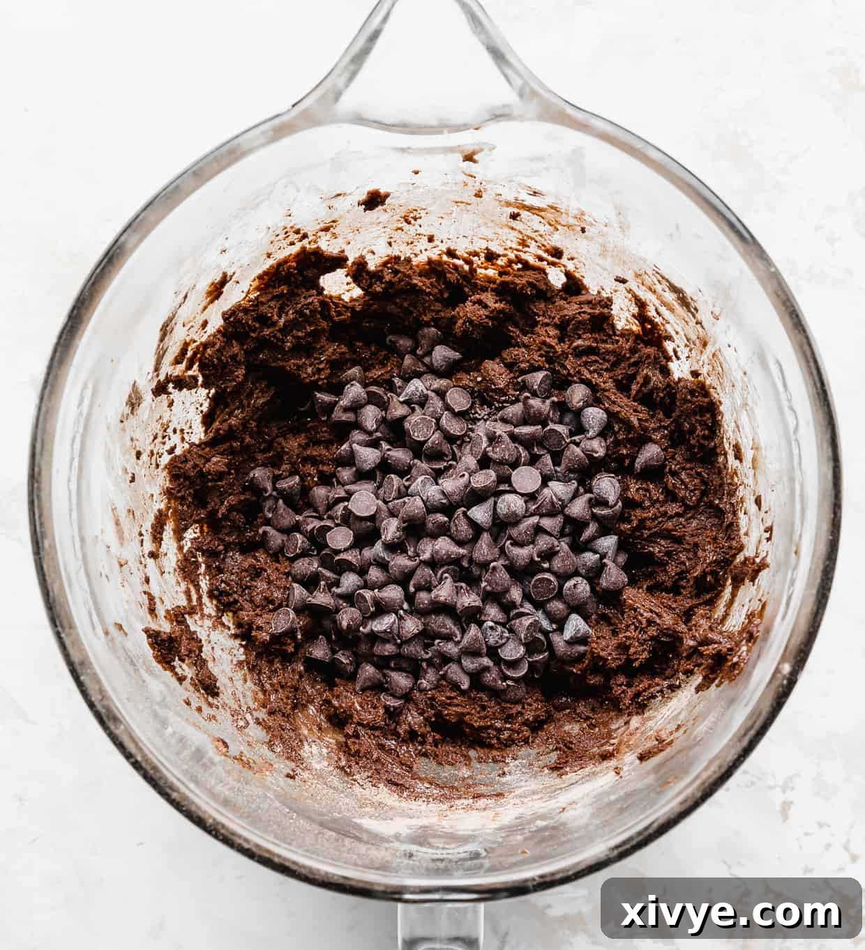 Double Chocolate Chip Cookie dough in a stand mixer bowl with chocolate chips overtop of the dough, ready for scooping.