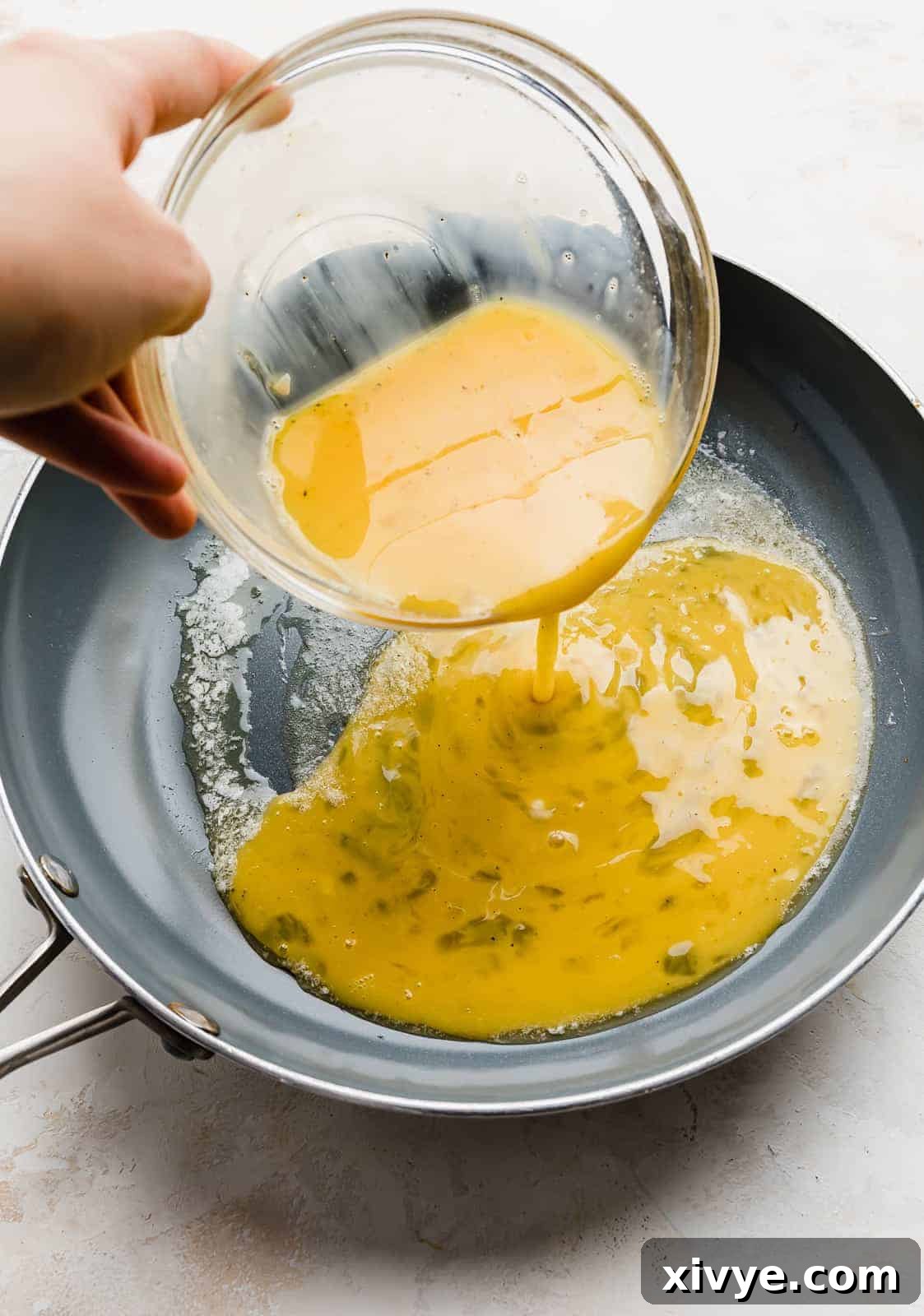 Gooey Cheese Scramble 5 A whisked egg mixture being poured into a gray nonstick skillet with melted butter.
