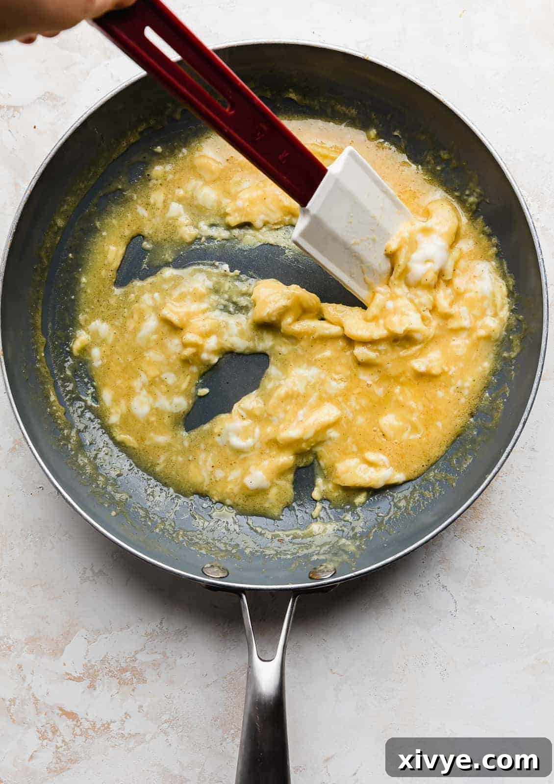 Gooey Cheese Scramble 6 A spatula stirring a scrambled egg mixture in a skillet, forming soft curds.