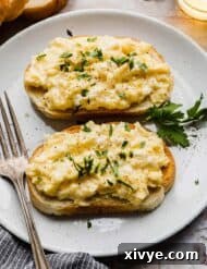 Two slices of bread topped with scrambled eggs and garnishes of chopped parsley.