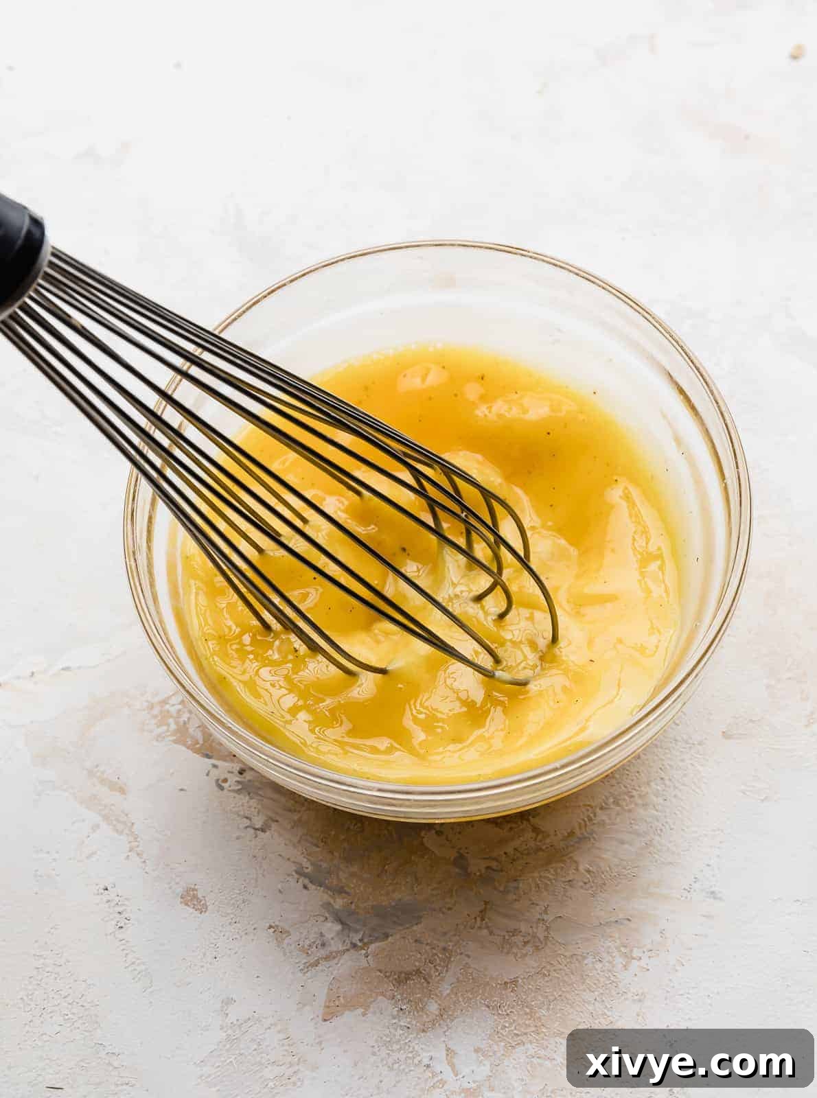 A whisk stirring an egg mixture in a glass bowl.