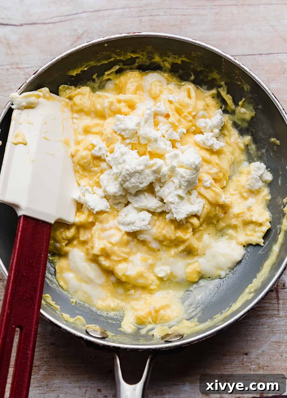 Crumbled white goat cheese overtop Scrambled Eggs in a skillet.