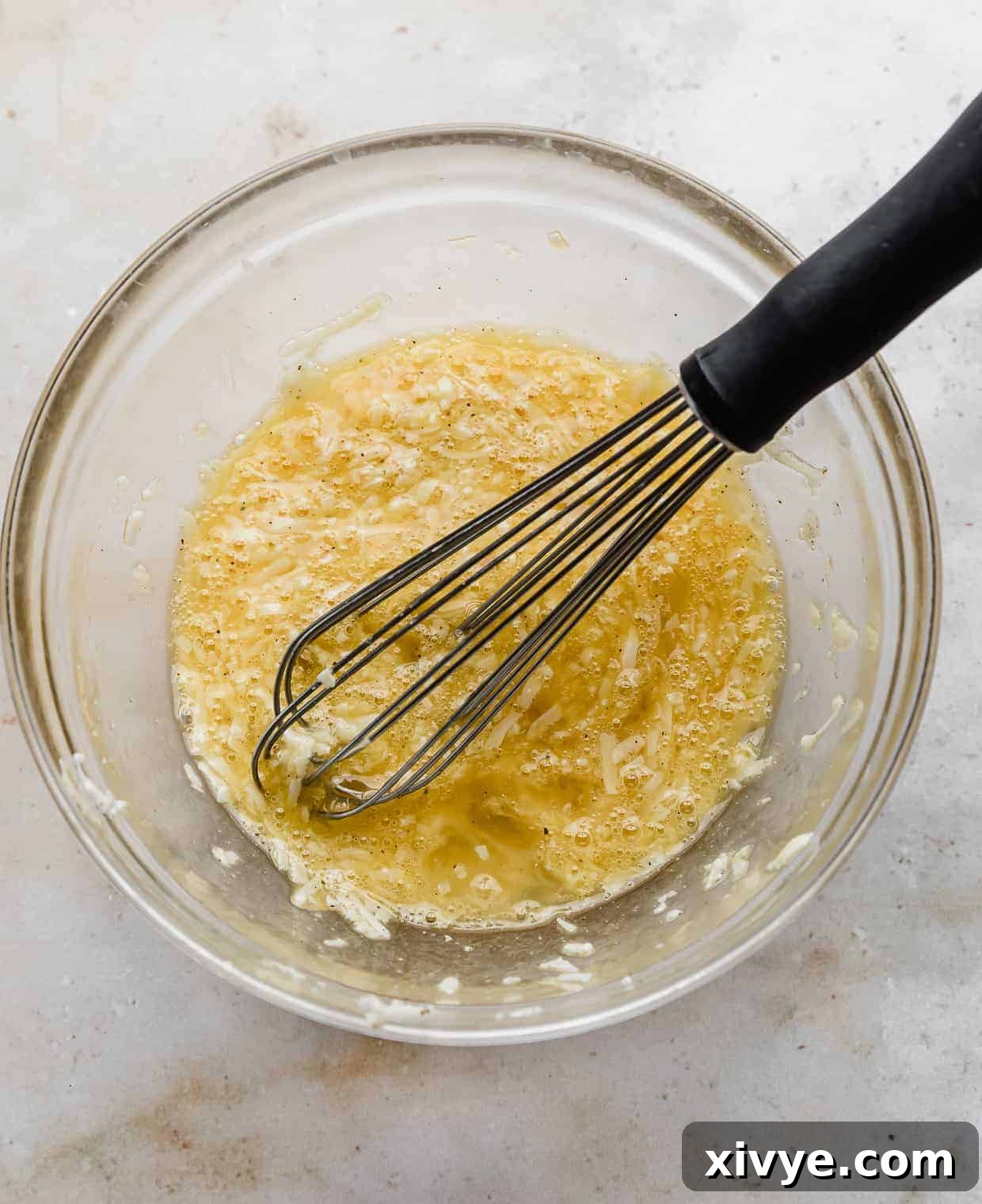 A whisk in a glass bowl with a yellow egg mixture.