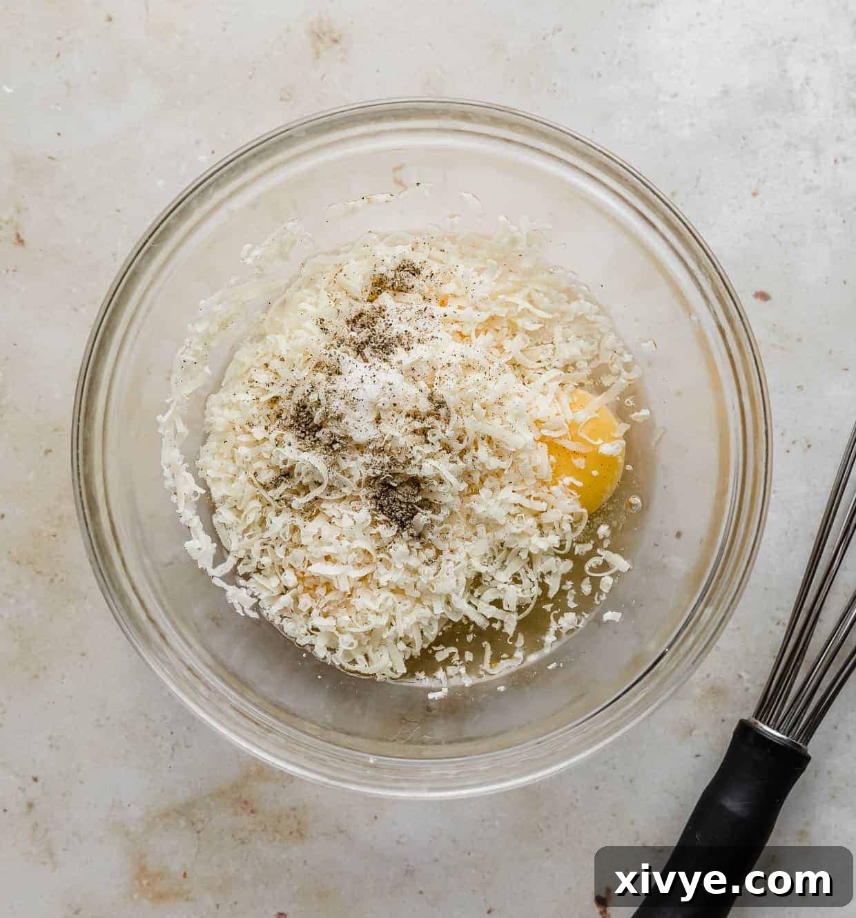A glass bowl filled with grated parmesan, cracked eggs, and seasonings.