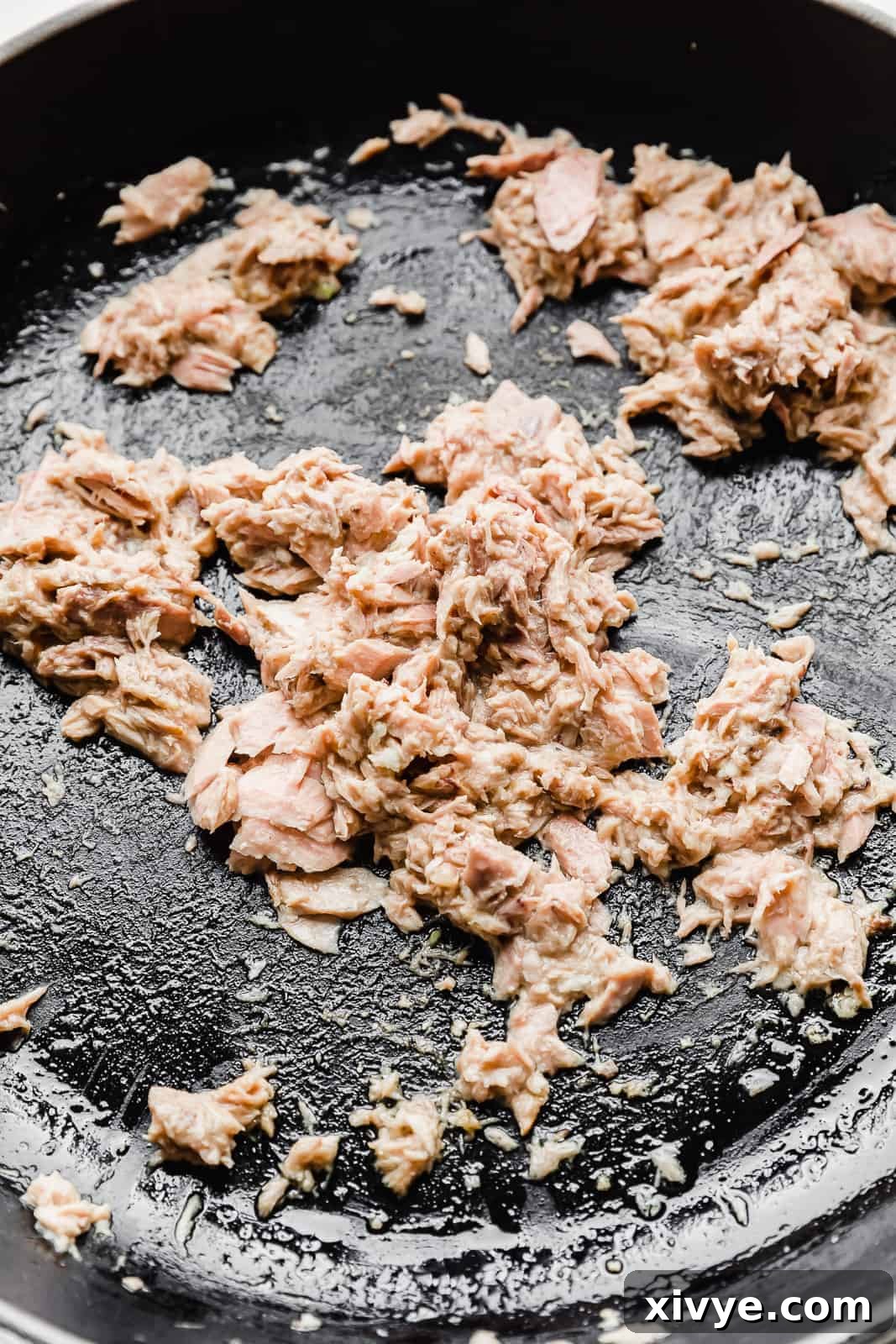 Canned tuna being cooked in a black skillet.