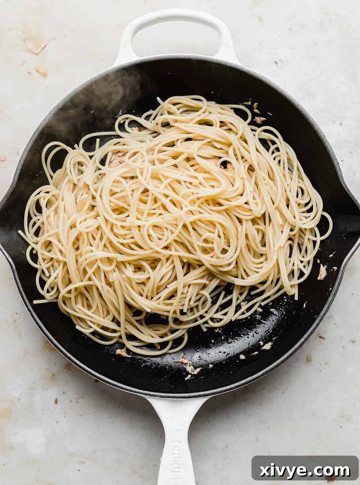 Spaghetti noodles in a black skillet on a marbled background.