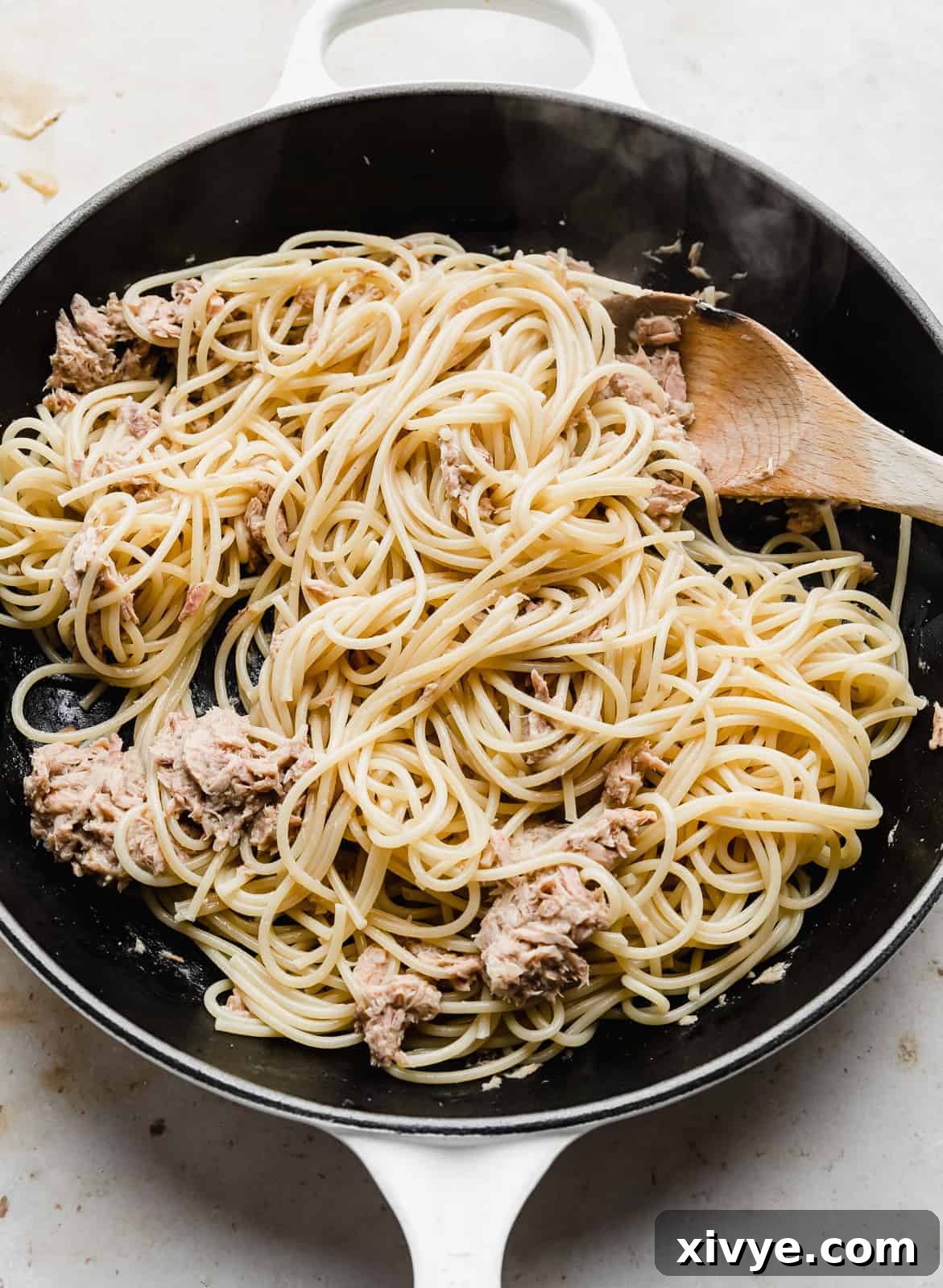 A wooden spoon stirring Tuna Carbonara in a skillet.