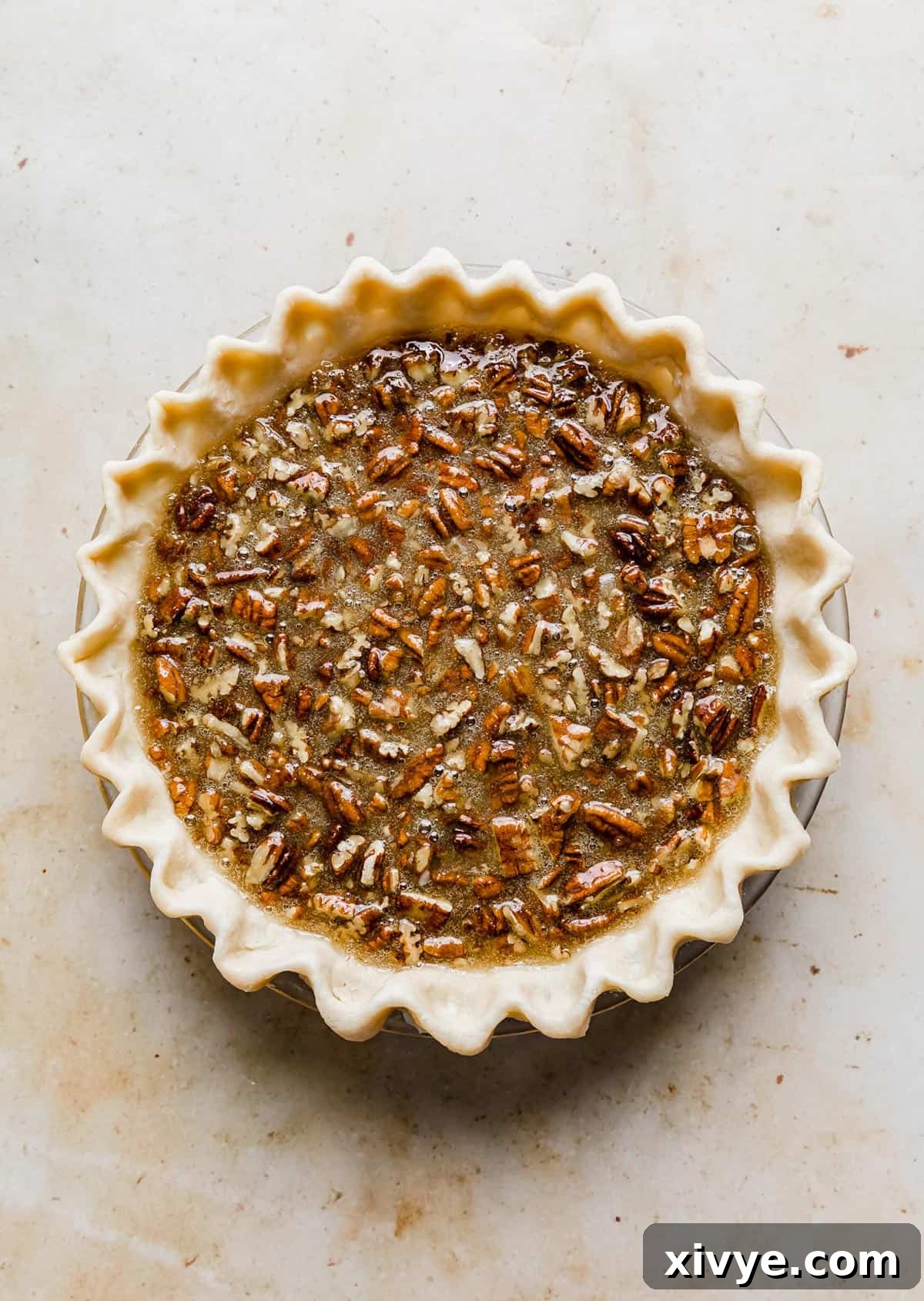 Ultimate Southern Pecan Pie 7 An unbaked southern pecan pie on a cream colored background.