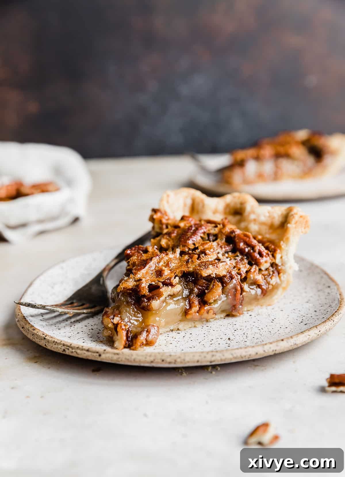Ultimate Southern Pecan Pie 9 A slice of Southern Pecan Pie on a white plate with a fork to the side of the pie.