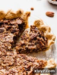 Ultimate Southern Pecan Pie 10 A pecan pie on a white background with pecan pieces in the background.