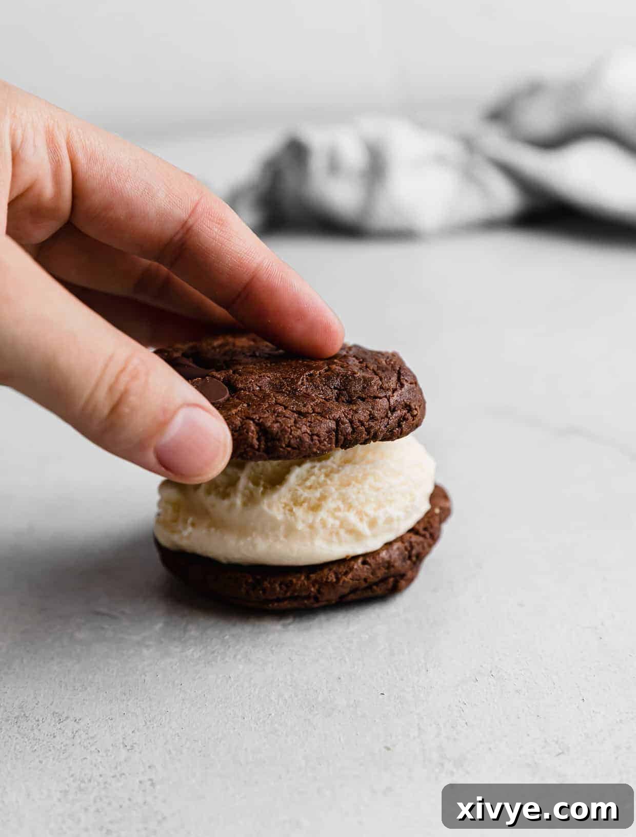Cookie Ice Cream Delight 9 A hand pressing a chocolate cookie on top of a scoop of ice cream.
