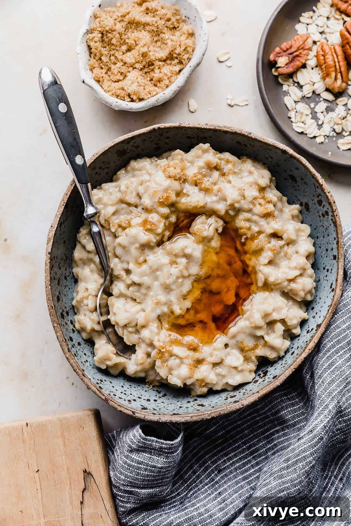 Golden Maple Oat Sweetness 7 A bowl of Maple and Brown Sugar Oatmeal on a cream background with a bowl of pecans and brown sugar to the side.