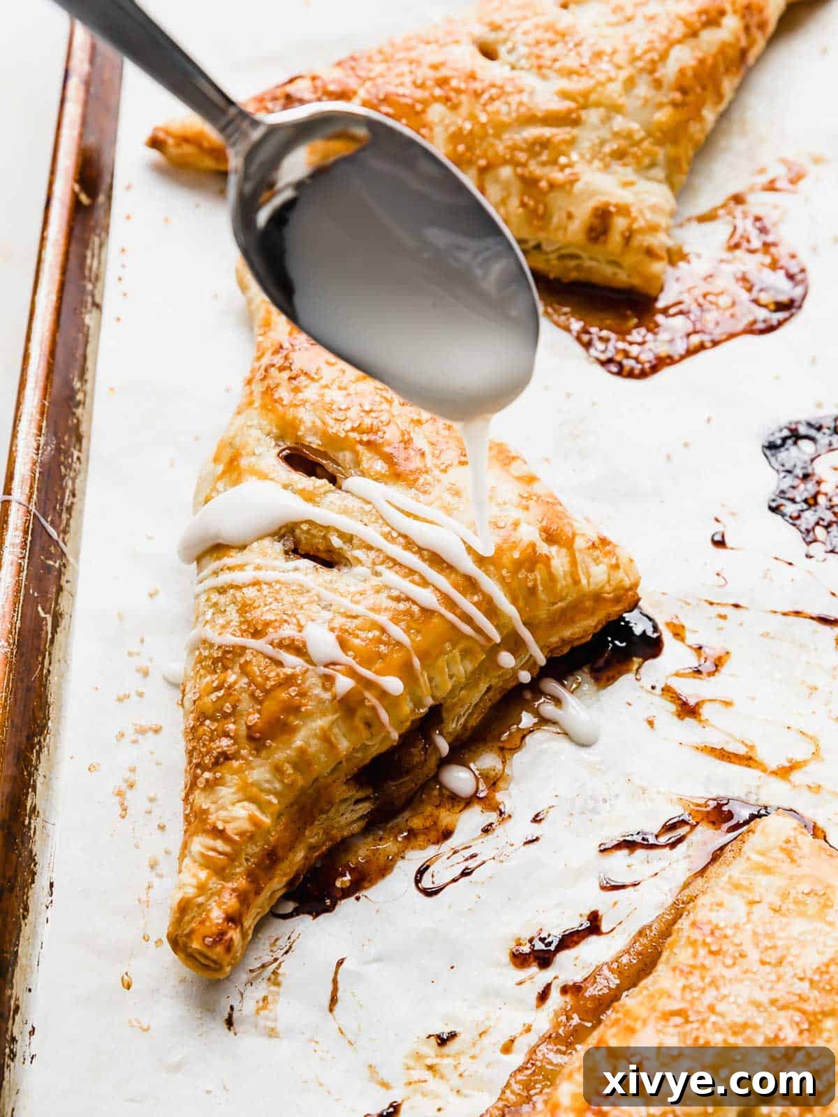 A spoon drizzling glaze overtop a Puff Pastry Apple Turnover.