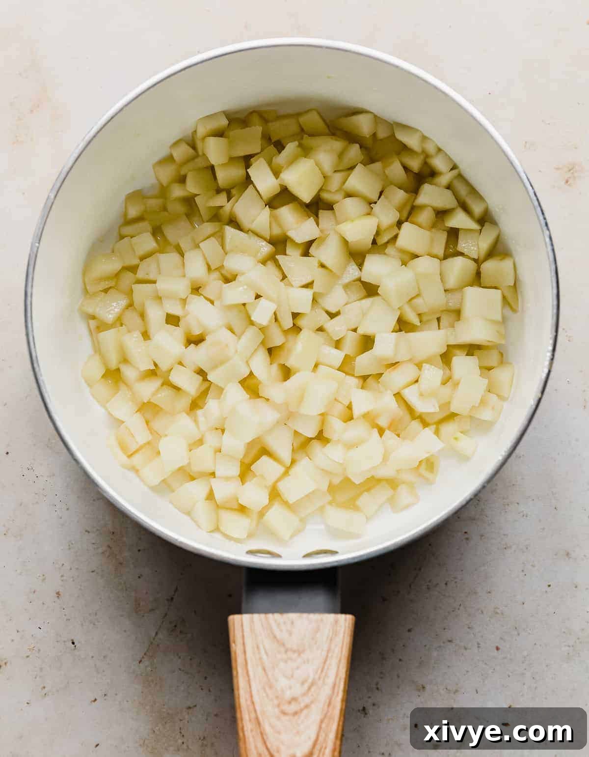 Softened diced apples in a white saucepan.