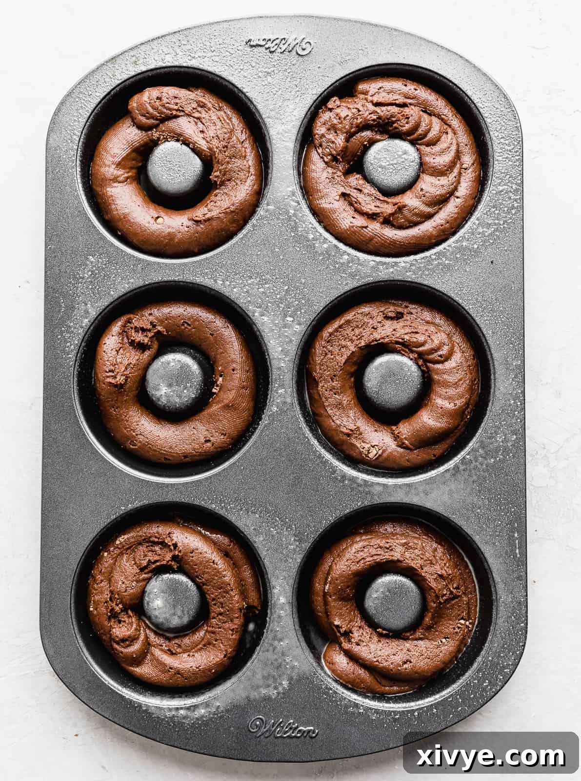 A donut pan with chocolate batter in each donut cavity.