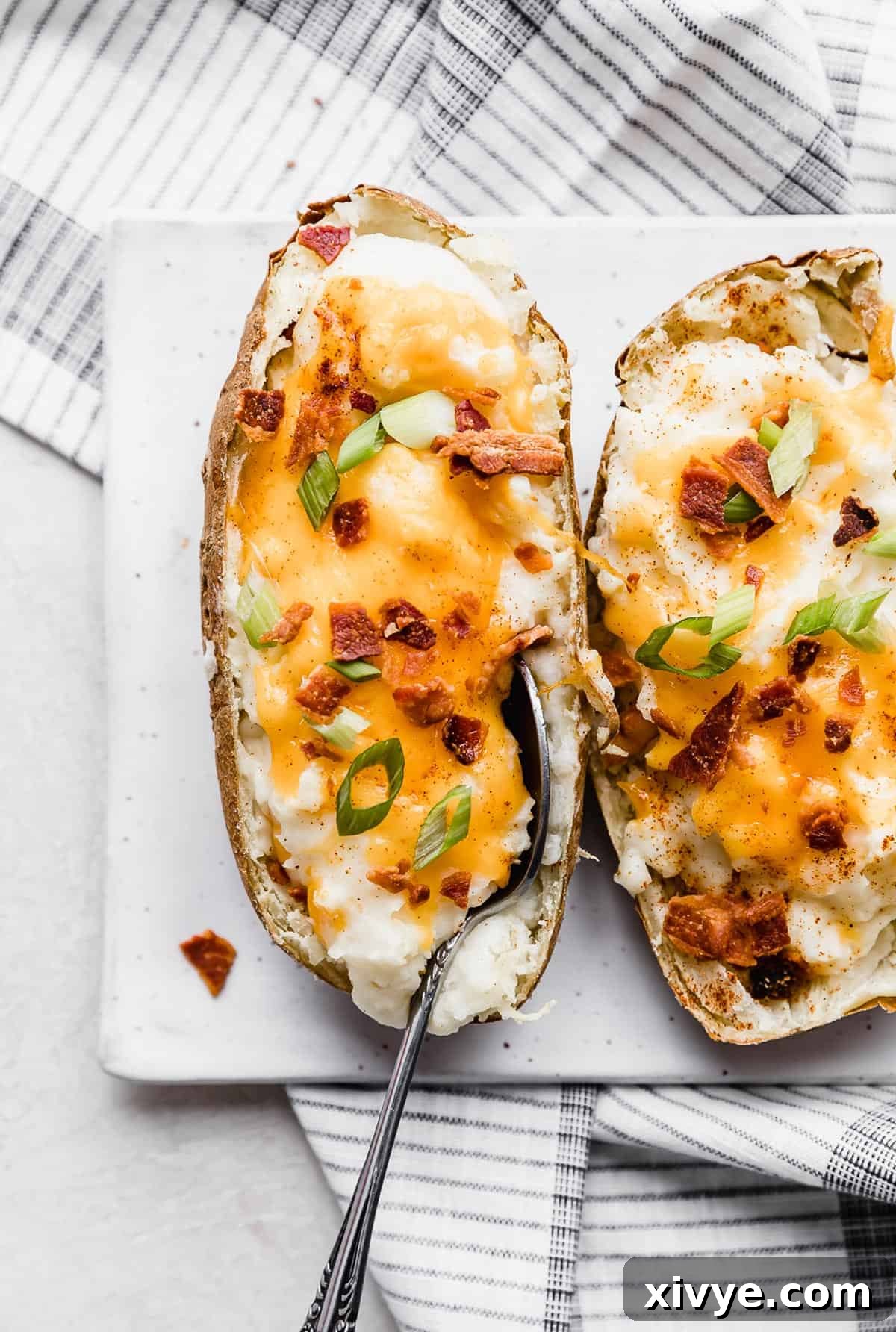 Decadent Double-Baked Potatoes 13 A Twice Baked Potatoes with Cream Cheese topped with orange cheese and crispy bacon, on a white plate.