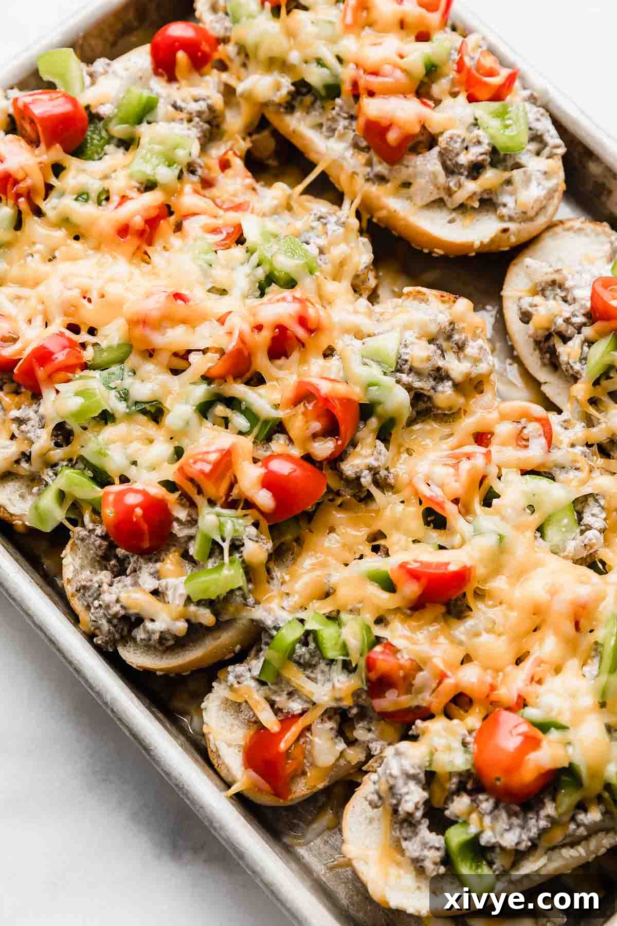 Beef Stroganoff Sandwiches on a baking sheet, each hoagie bun topped with ground beef mixture, diced tomatoes and green peppers, and melted cheddar cheese.