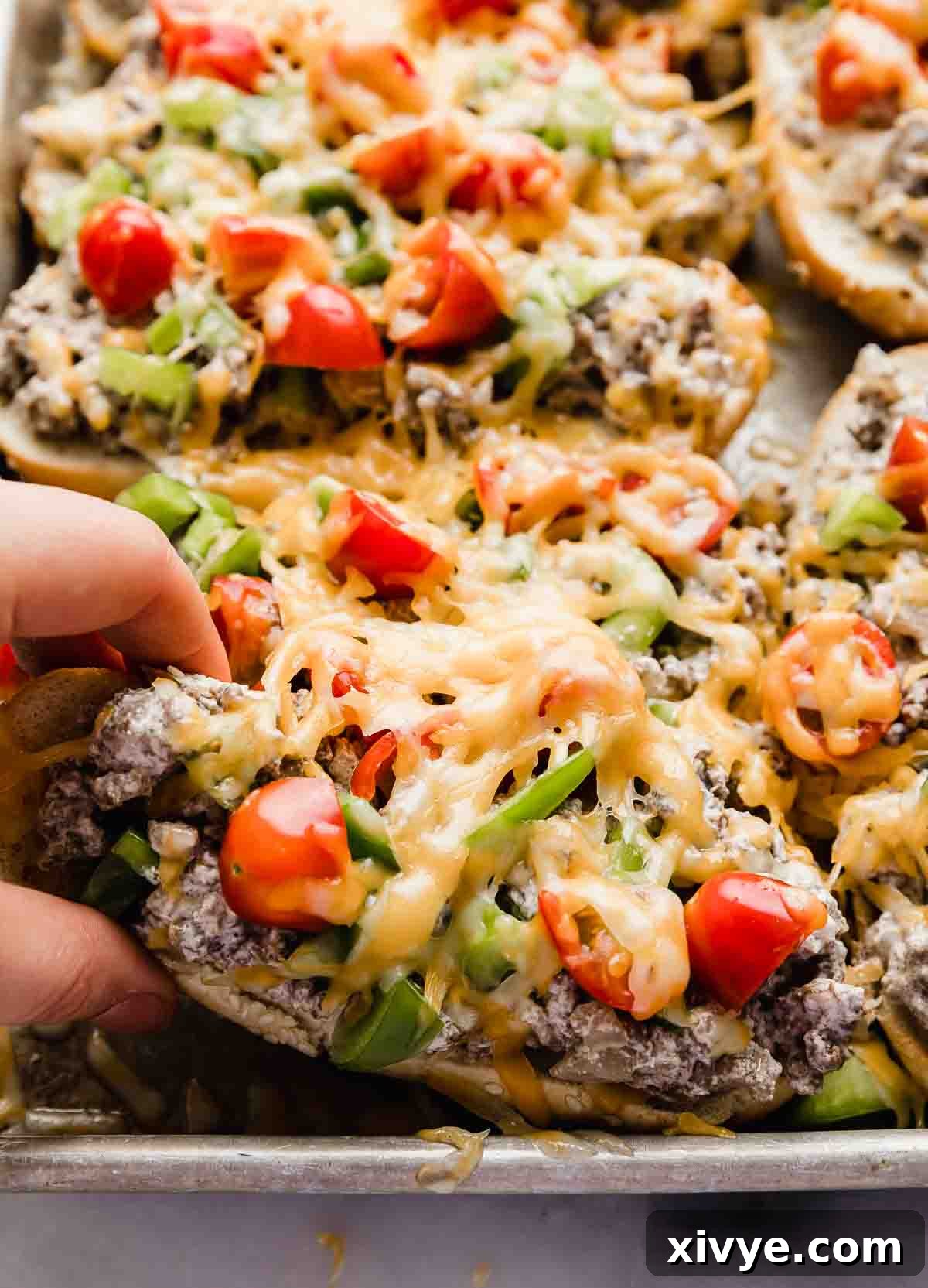 A hand grabbing a Beef Stroganoff Sandwich that's topped with ground beef, tomatoes, peppers, and shredded melted cheese.