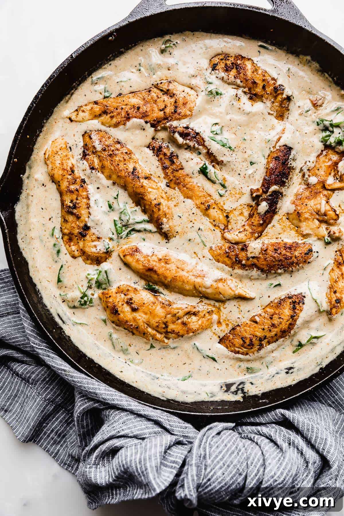 A black cast iron skillet full of a Creamy Tuscan Chicken Recipe swimming in a tan colored gravy.