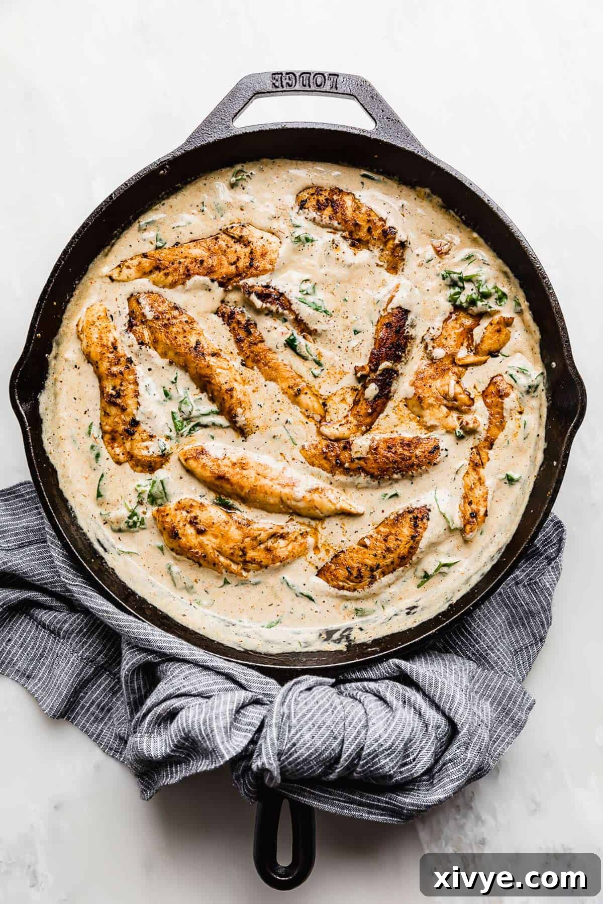 Creamy Tuscan Chicken Recipe in a skillet on a white background.