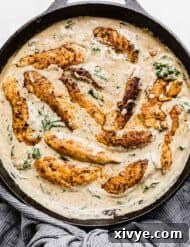 Creamy Tuscan Chicken in a black skillet with sun dried tomatoes and spinach in the sauce.