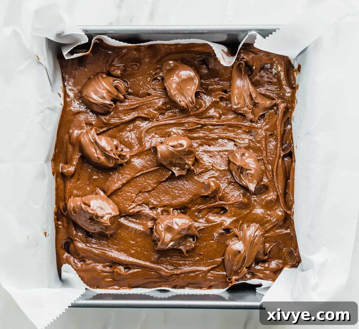 Decadent Nutella Hazelnut Brownies 5 Nutella Brownie batter in an 8x8 pan, with dollops of Nutella along the top, ready for swirling.