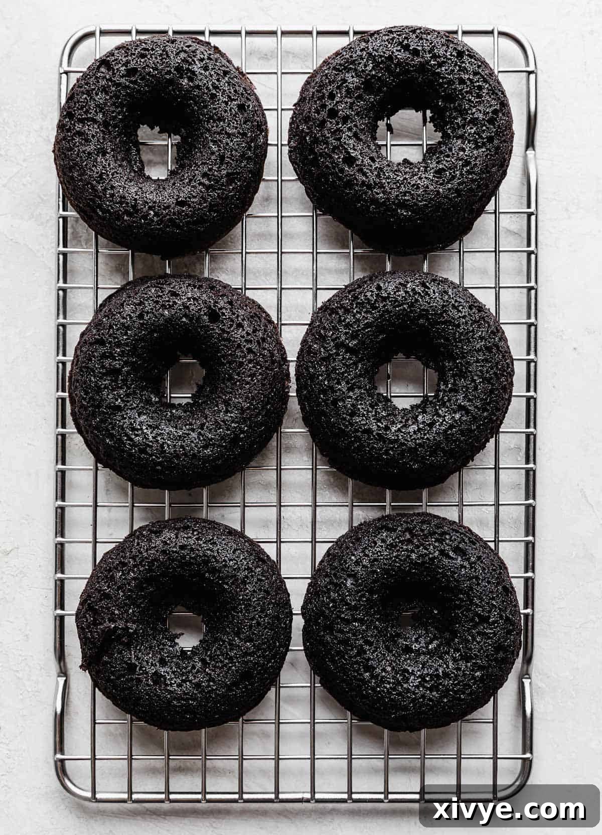 Six baked Oreo Donuts cooling on a wire rack, showing their perfect shape and dark color.