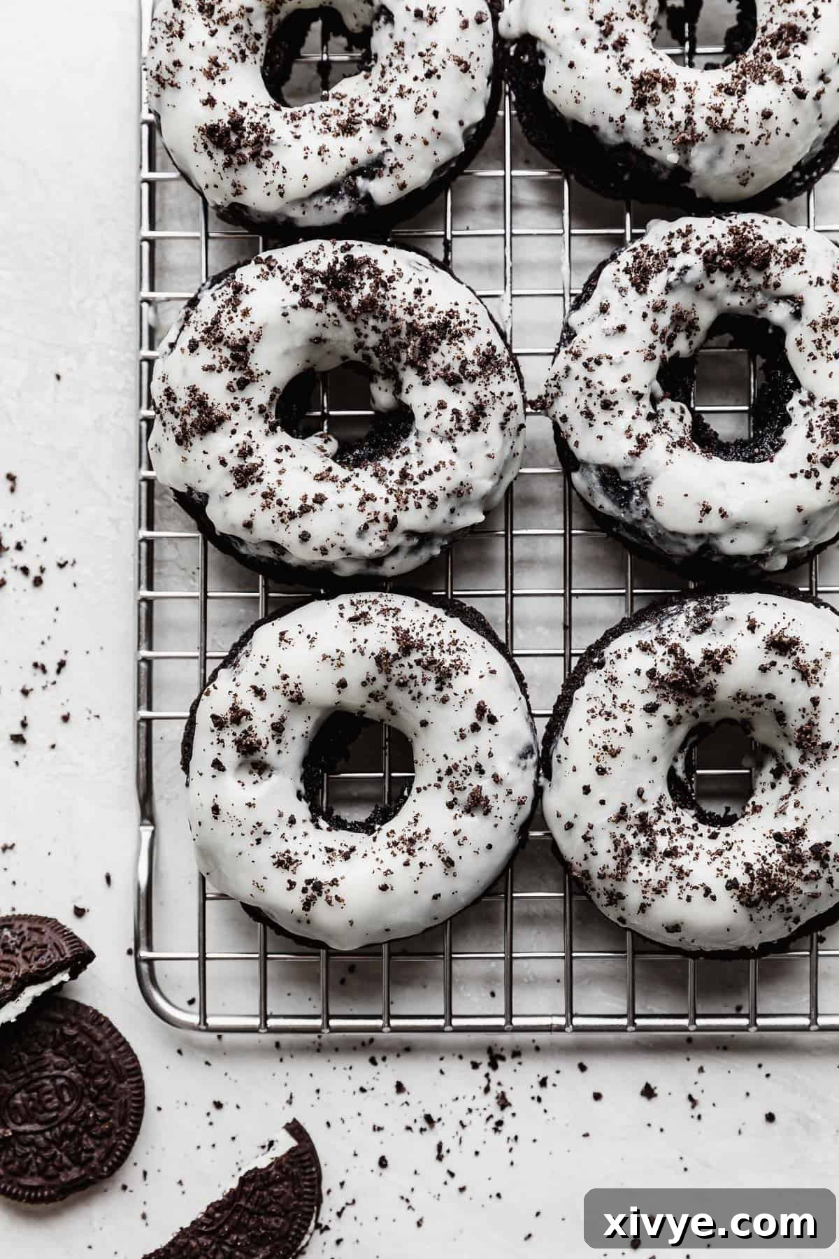 White frosting topped Oreo Donuts with crushed Oreo crumbs, arranged on a wire rack, showcasing the final delicious product.