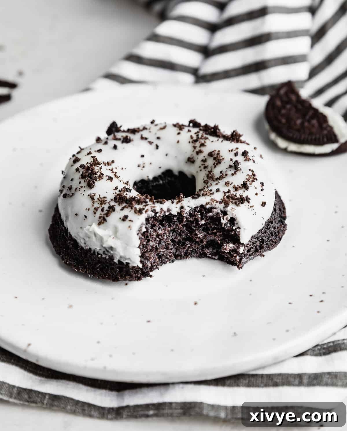 An Oreo Donut on a white plate with a bite taken out of it, revealing the moist interior.