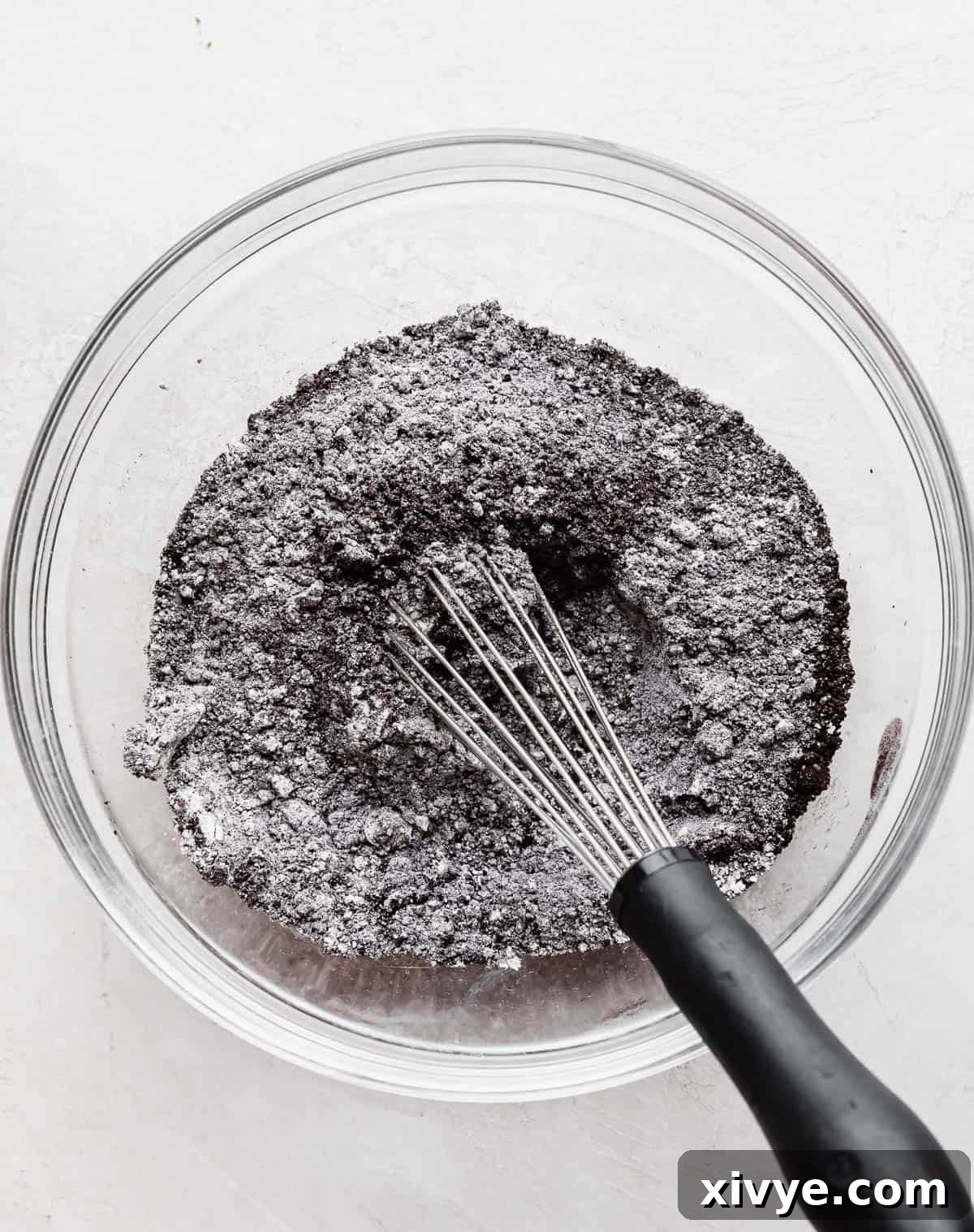 Dry ingredients for Oreo Donuts, including flour, black cocoa, and baking agents, mixed in a clear glass bowl.