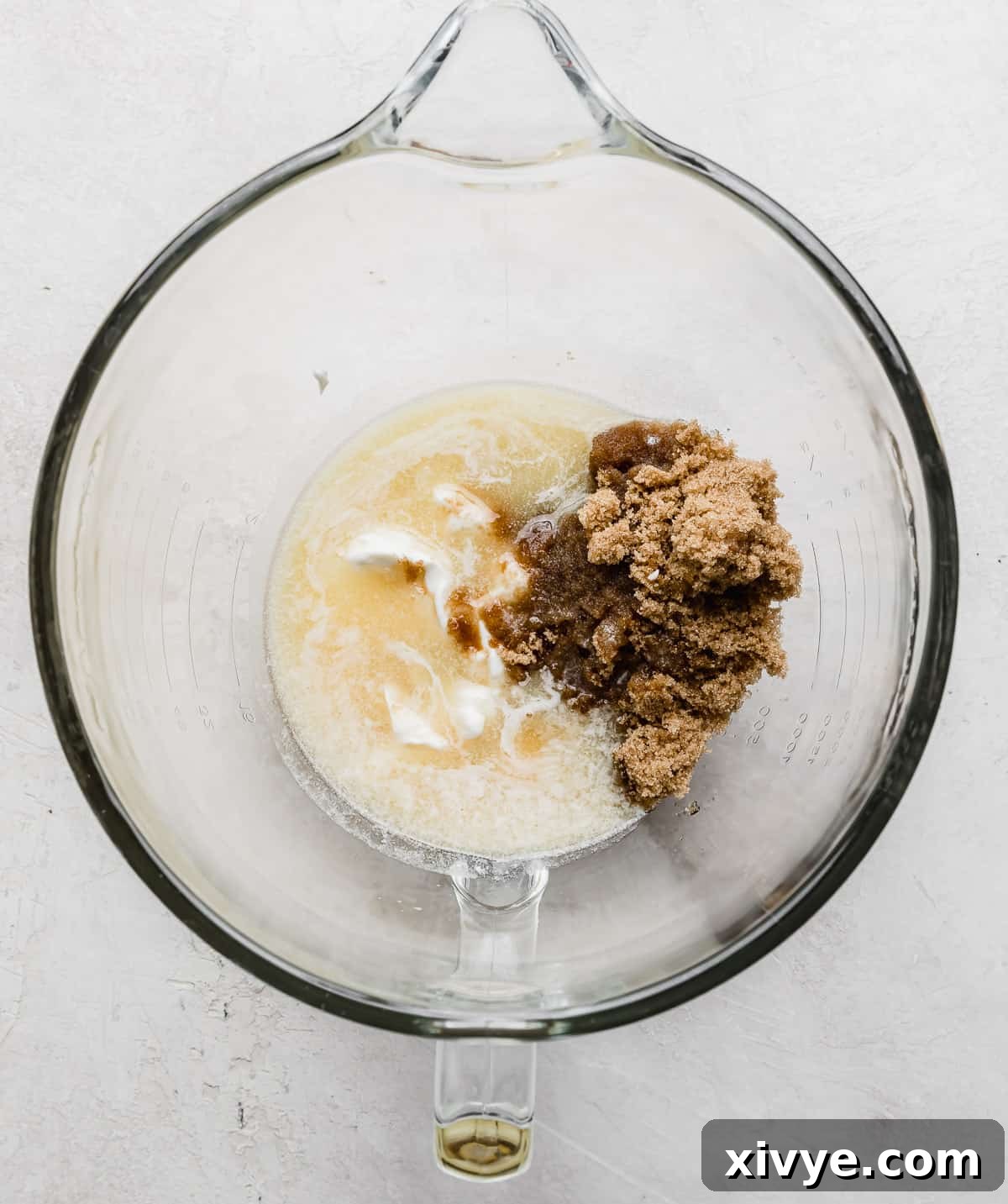 A glass bowl containing melted butter, brown sugar, and vanilla extract, ready to be mixed with other wet ingredients.