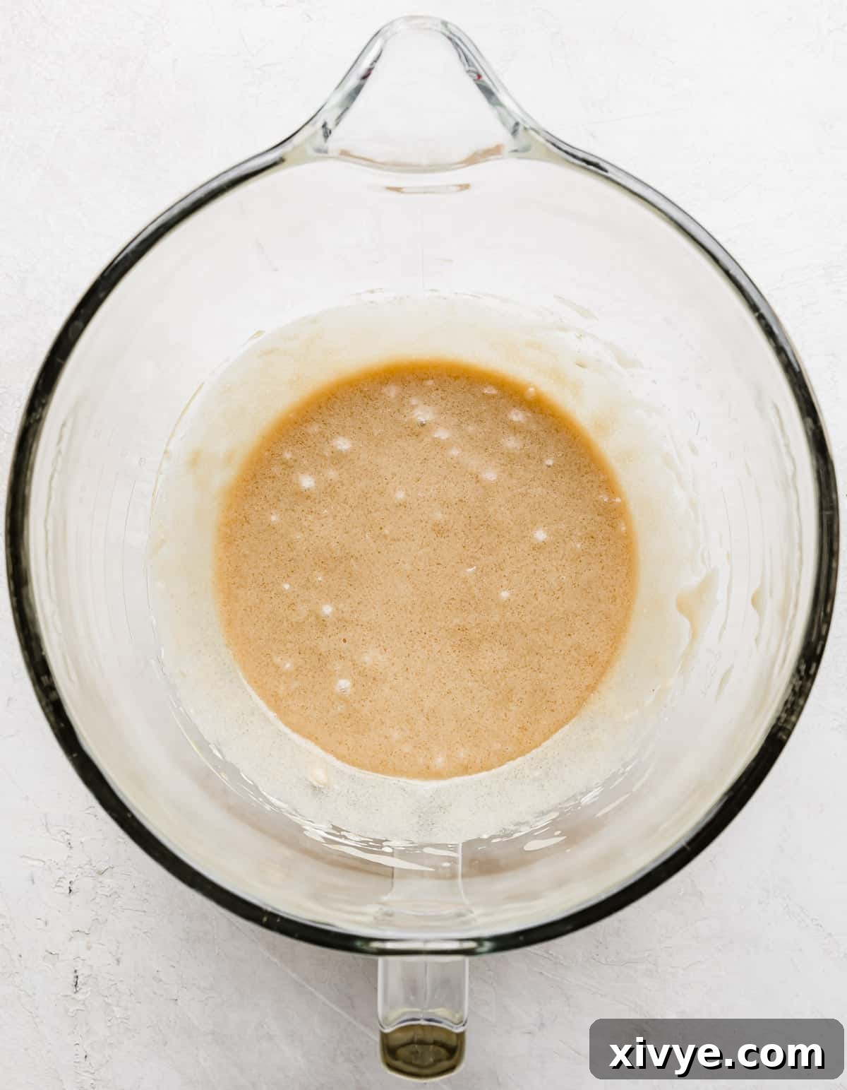 A tan-colored wet ingredient mixture, smooth and well-combined, in a glass mixing bowl, after all wet ingredients have been blended.