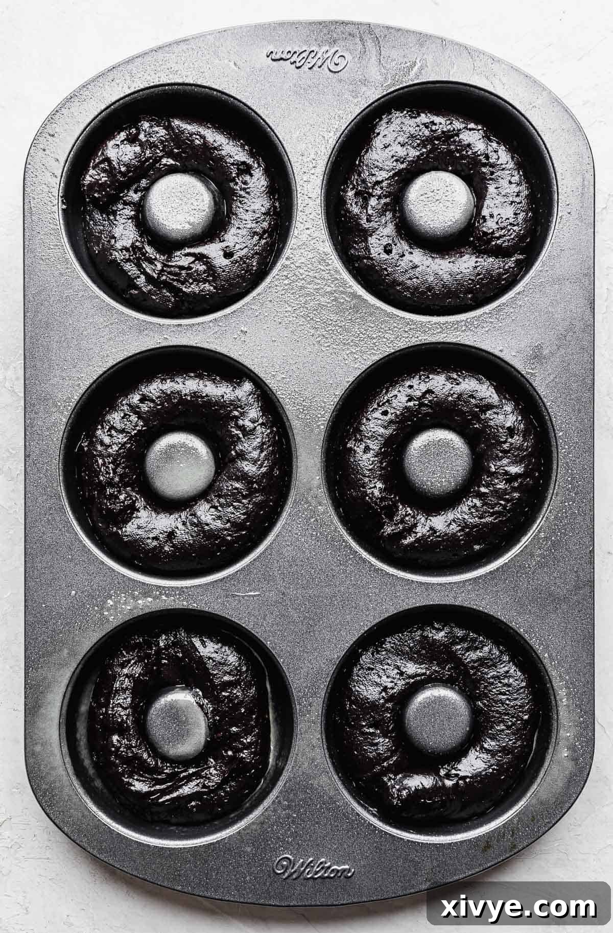 Oreo Donut batter neatly piped into a six-cavity donut pan, ready to go into the oven.