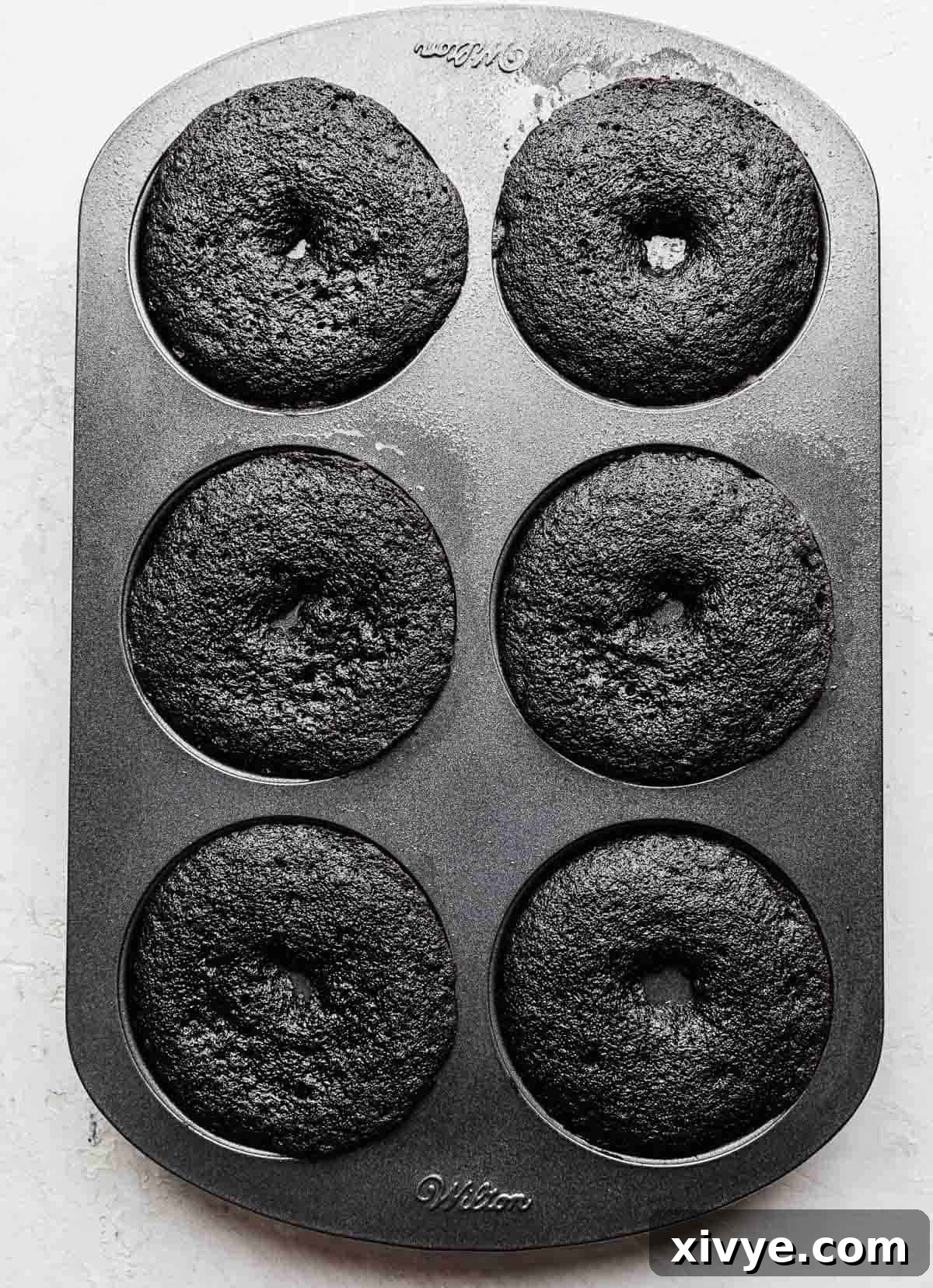 Freshly baked Oreo Donuts, golden brown and puffed, still in their six-cavity donut pan after baking.