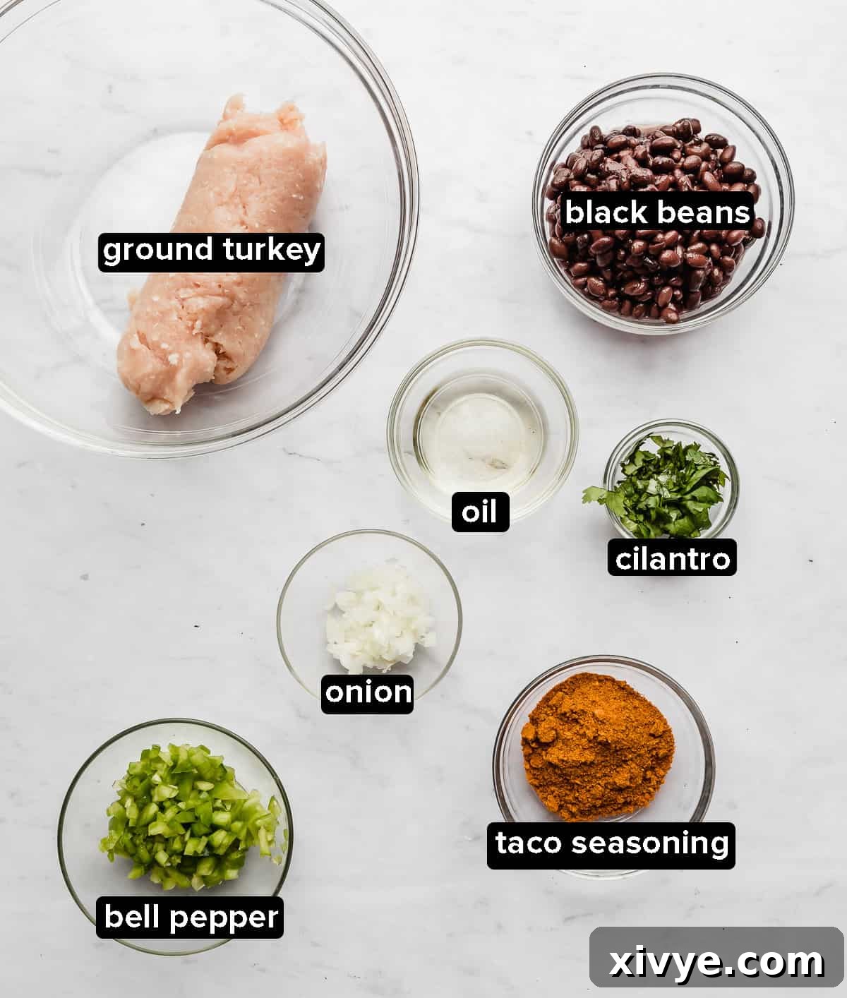 Fiesta Turkey Burgers 3 Individual ingredients for Taco Turkey Burgers arranged in glass bowls on a white background, including ground turkey, black beans, taco seasoning, and cilantro.