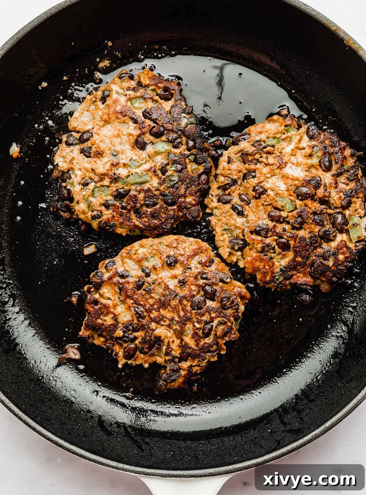Fiesta Turkey Burgers 7 Cooked Taco Turkey Burger patties, some topped with melted cheese, resting in a black skillet after cooking.