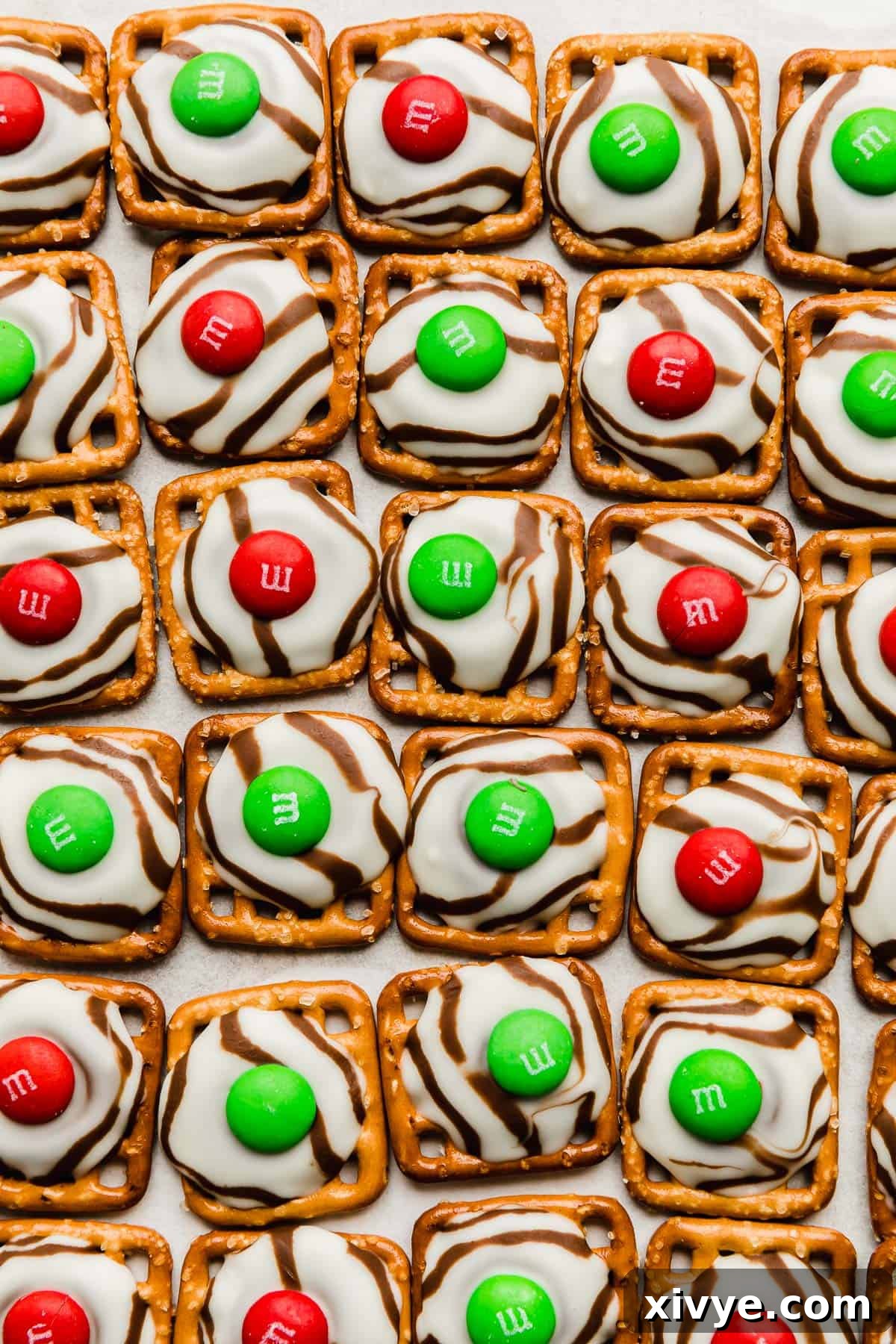 Yuletide Pretzel Bites 5 A close-up shot of square pretzels topped with gently melted Hershey's Hugs, each adorned with a festive red or green M&M, showcasing the perfect post-bake consistency.