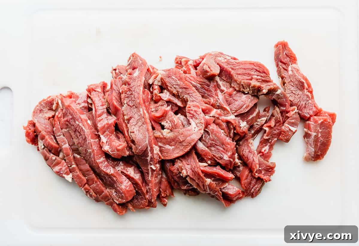 Flank steaks cut into thin strips on a white cutting board, showing how to cut against the grain.