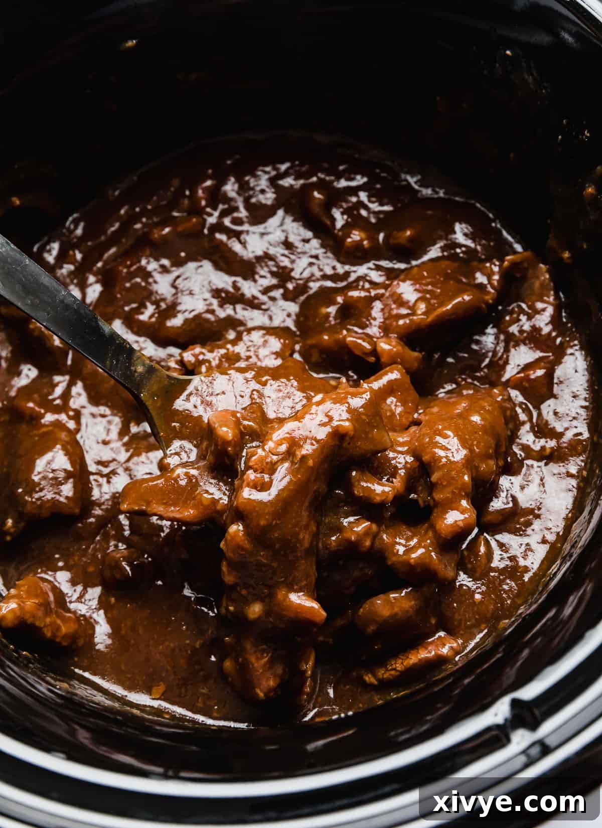 Slow Cooker Mongolian Beef in a black slow cooker, topped with fresh green onions, ready to be served.