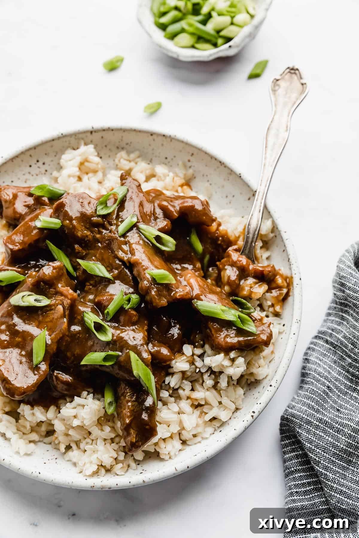 Slow Cooker Mongolian Beef on a bed of brown rice, with a fork taking a bite.