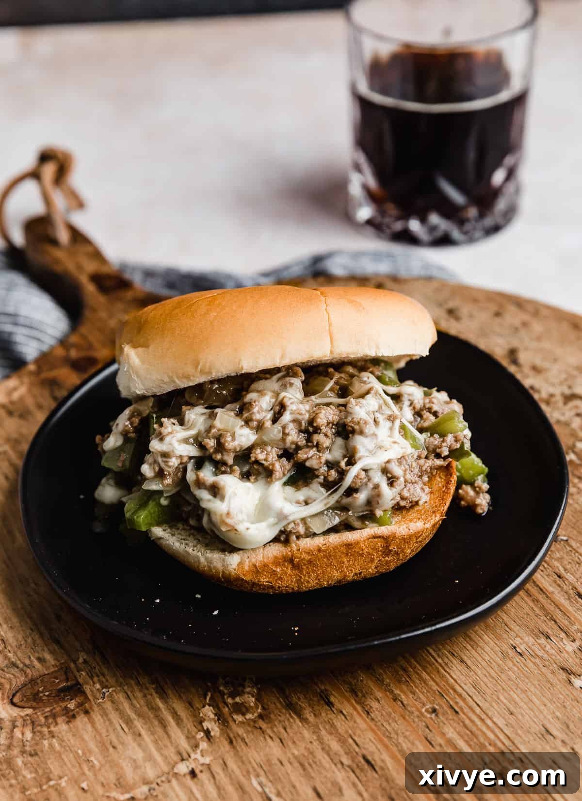Philly Cheesesteak Joes 2 A delectable Philly Cheesesteak Sloppy Joe on a black plate, resting on a rustic wooden cutting board, ready to be devoured.