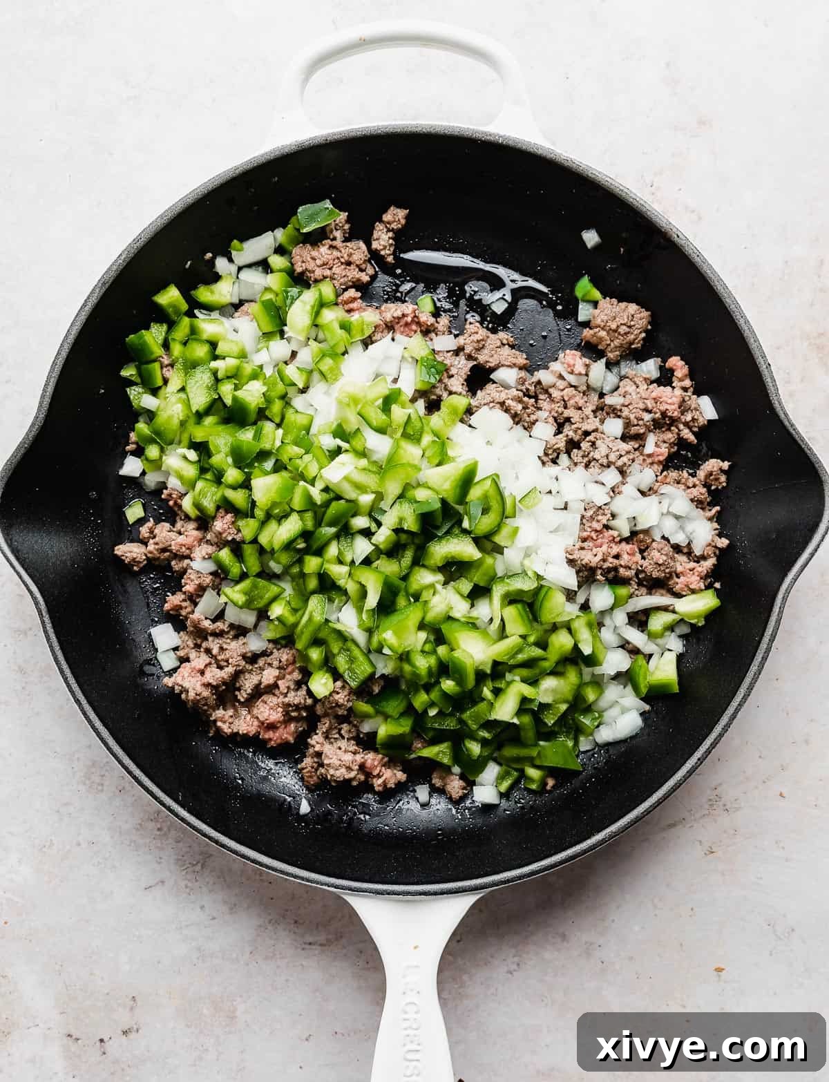 Philly Cheesesteak Joes 4 A white skillet with ground beef, finely chopped onion, and vibrant green peppers, capturing the initial stages of cooking.